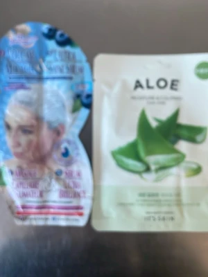 Ansiktsmas och Håtmask med blåbär och aloe vera - Två masker  i engångsförpackning, en med blåbärstema och en med aloe vera. Perfekt för återfuktning och lugnande effekt. Maskerna är i färgglada förpackningar, en blå och en vit med gröna detaljer.