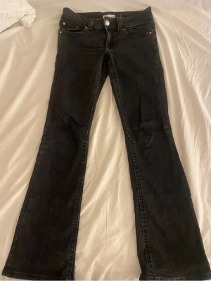 Svarta bootcut jeans från Gina tricot  - Säljer ett par svarta bootcut jeans från Gina med klassisk femficksdesign och snygga bakfickor med lock och knapp. Jeansen har låg midja och är tillverkade i mjukt denimtyg med stretch för extra komfort. Perfekta till sneakers eller boots.