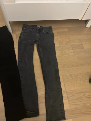 Svarta och grå jeansbyxor - Två par jeansbyxor i svart och mörkgrå färg, båda med klassisk femficksdesign och raka ben. Jeansen är tillverkade i bomullsmaterial och har knapp- och dragkedjestängning. Passar dig som gillar en enkel och stilren look.