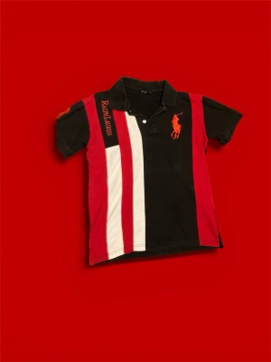 Pikétröja från Polo Ralph Lauren - Snygg pikétröja från Polo Ralph Lauren i svart, rött och vitt med breda ränder. Stor röd broderad logga på bröstet oh siffran 3 på ärmen. Klassisk krage och knappar framtill. Materialet är mjuk bomull och tröjan har en normal passform.