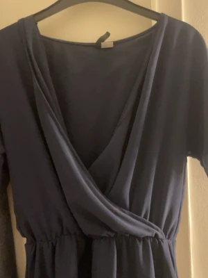 Mörkblå omlott byxdress från Divided - Säljer en mörkblå byxdress från Divided i storlek 36. Byxdressen har omlottringning, resår i midjan och fina spetsdetaljer längst ner. Materialet är mjukt och faller snyggt. Perfekt för dig som gillar en enkel men ändå chic stil.