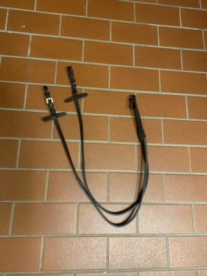 Brun lädertygel med gummigrepp💕 - Säljer ett par bruna tyglar i läder med mässingsspännen och gummigrepp på insidan för extra fäste. Perfekt för ridning och passar till träns. Snygg och stilren design som funkar till de flesta träns. Storlek ponny, säljer för att dem var får korta/små💕 bara testade! Köparen står för frakten!