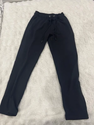 Svarta mjukisbyxor med snörning - Svarta mjukisbyxor med elastisk midja och snörning framtill. Byxorna har raka ben och är tillverkade i ett mjukt material som känns skönt mot huden. Perfekta för chill dagar eller när du vill ha det bekvämt.