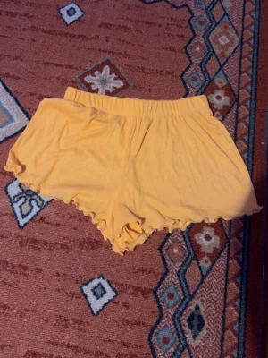 Orangea volangshorts - Säljer ett par orangea shorts från Primark i storlek XS. De har elastisk midja och volangkant nedtill för en söt vibe. Tillverkade i mjuk bomull, perfekta för varma dagar eller som chill-plagg hemma. Köpta i Spanien av släkt så har ingen aning vad de kostade. Använt ett fåtal gånger. Säljes då jag har för många pyjamas shorts och använder aldrig dessa. Jätte sköna. 