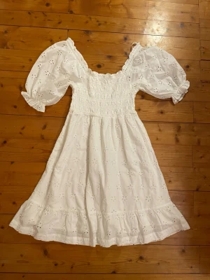 Vit broderad sommarklänning XS - Supersöt vit klänning i bomull med broderade blommor och puffiga korta ärmar. Perfekt till studenten, skolavslutningen eller midsommar! Säljes i storlek XS. Använd 1 gång🫶