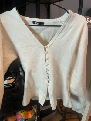 Vit kofta med knappar från Gina Tricot - Supersöt vit kofta från Gina Tricot i storlek XS. Koftan har v-ringning, långa ärmar och dekorativa tygklädda knappar framtill. Materialet känns mjukt och lite tjockare, perfekt för lager på lager under höst och vår.