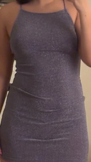 Glittrig lila kortklänning - Säljer en glittrig lila kortklänning med tunna axelband som korsas i ryggen. Klänningen har en tight passform och är ärmlös, perfekt för dig som vill sticka ut. Materialet känns mjukt och stretchigt, och den skimrar snyggt i ljuset.