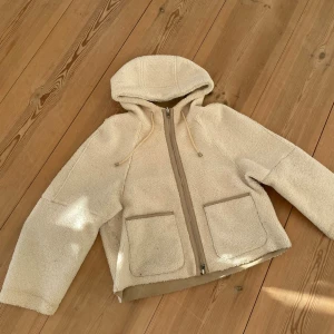 Teddyjacka med huva från Oui - Säljer en teddyjacka och mockajacka från Oui med huva och snörning. Jackan går att vända åt båda hållen och har två stora fickor framtill och dragkedja. Modellen är loose fit. Inköpt på Sandhamn för 3000 kr🩷
