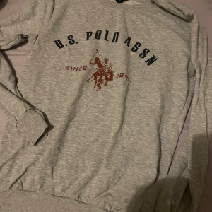 Grå sweatshirt från Polo Sport - Grå sweatshirt från Polo Sport Ralph Lauren med tryck framtill av polospelare och texten U.S. POLO ASSN. Tröjan har rund hals, långa ärmar och ribbade muddar. Perfekt för en chill och sportig look.