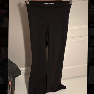 Svarta bootcut träningsbyxor RS Sports - Svarta bootcut träningsbyxor från RS Sports med hög midja och stretchigt material. Perfekta för dig som gillar en bekväm och snygg look på gymmet eller till vardags. Sitter tajt upptill och släpper ut vid benen för en trendig siluett😇