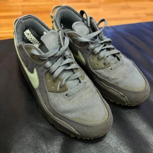 Nike Air Max 90 x Pass~Port grå/oliv - Nike Air Max 90 x Pass~Port i grått och olivgrönt med canvas- och mockadetaljer. Swoosh i ljusgrönt, robust sula och klassisk Air Max-dämpning. Skorna har snörning och coola kontrastdetaljer, perfekta för dig som gillar streetwear och unika samarbeten.