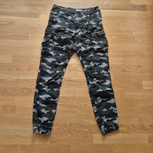 Kamouflagemönstrade cargobyxor * Stl S herr - * Kamouflagemönstrade cargobyxor. * Stl S herr. Passar M/L dam. * Midjemått mätt rakt över: ca 80 cm. * Mått innerben: ca 78 cm * Total längd: ca 101 cm * Resår i benslut och förstärkta i innerlår.  * 98% bomull, 2 % elastan * Jättebra skick. Hittar inga skavanker.  Djur och rökfritt hem. Se bilder och förstora då de ingår i beskrivningen. Se gärna mina övriga annonser.  Vid avhämtning finns de i Sollentuna.