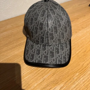 Grå mönstrad keps från Dior - grå keps från Dior med ett all-over logomönster och svarta detaljer runt skärmen.