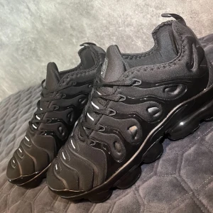 Nike Air Vapormax Plus helsvarta sneakers - Hej, Säljer nu mina Nike Air Vapormax Plus i helsvart storlek 43. Har använt dem en gång på en utekväll med vänner. Märkte att dom va för stora med då var det tyvärr sent då jag redan hade haft på mig dem ute, sen dess har dom legat hemma på skohyllan. Tänkte det blir onödigt att kasta dem när man kan få en liten slant pengar. Det finns inga skador på dem, och dem ser helt nya ut.