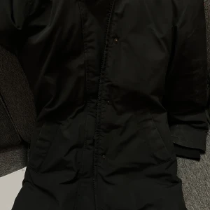 Svart parkas från Canada Goose XS - Svart lång parkas från Canada Goose med huva och klassisk logga på ärmen. 