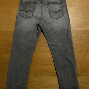Grå jeansbyxor (Replay) - Snygga grå jeansbyxor från replay med klassiska fem fickor. Byxorna har svarta detaljer på bakfickorna och en diskret tvättad look. Perfekta för en avslappnad stil och passar till det mesta.
