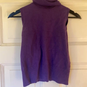 Lila ärmlös polotröja i ull  - En lila väst med polokrage och bred ribbad kant nedtill. Bra skick i storlek XS/S med en viss defekt vid ärmarna, se bild 