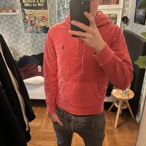 Rosa hoodie från Polo Ralph Lauren - Snygg rosa hoodie från Polo Ralph Lauren med klassisk blå logga på bröstet. Tröjan har huva med snörning, magficka och långa ärmar. Mjuk bomullskvalitet som är skön att ha på sig. Givetvis äkta!