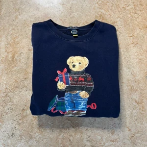 Mörkblå Polo Bear tröja Ralph Lauren - Snygg mörkblå sweatshirt från Ralph Lauren med Polo Bear-tryck på framsidan.  Storlek xl i barn så passar s i vuxen ca 170-180. Bra skick förutom ett litet hål vid bröstet som knappt syns.