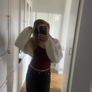 Vit croppad stickad kofta - Säljer en vit croppad stickad kofta med vida ärmar. Koftan är öppen framtill och har en riktigt mysig och trendig look. Perfekt att slänga över ett linne eller topp för en chill vibe. Superenkel att styla till olika outfits!