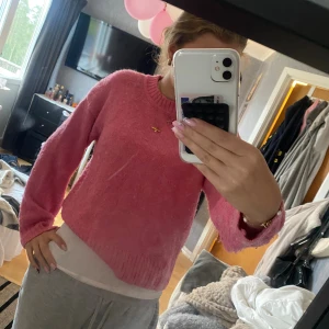 Rosa stickad tröja med rund hals - Mysig rosa stickad tröja med rund halsringning och ribbade muddar vid ärmslut och nederkant. Tröjan har en enkel och klassisk design som är lätt att matcha med olika outfits. Perfekt för kyligare dagar när du vill vara både bekväm och snygg.