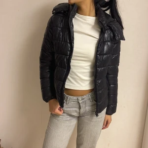 Svart pufferjacka med huva - Snygg svart pufferjacka med glansig finish och huva. Jackan har dragkedja framtill, två sidofickor och quiltad design. Köpt för 350kr🙌🏼