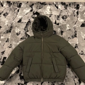 Olivgrön pufferjacka från Bershka - Säljer en olivgrön pufferjacka från Bershka i storlek S men kan passa M . Jackan har huva med snörning, två sidofickor och dragkedja framtill. Perfekt för vintern Den är quiltad och har en loose passform med långa ärmar, perfekt för kalla dagar. Skriv gärna för mer