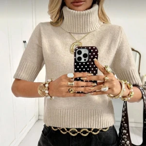 Beige polotröja i kashmirlook - Trendig beige polotröja med korta ärmar och bred ribbad krage. Tröjan har en croppad passform och är stickad i ett mjukt material som påminner om kashmir. Använd en gång