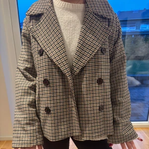 Rutig skepparkavaj från Object - Snygg rutig skepparkavaj från Object i bruna, svarta och vita toner. Jackan har dubbelknäppning med stora knappar, bred krage och en loose passform. Nypris 85å