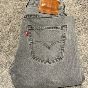 Grå Levi's 501 jeans W28 L32 - Säljer ett par klassiska grå Levi's 501 jeans med raka ben och femficksmodell. Jeansen har den ikoniska läderpatchen bak i midjan och röd Levi's-tagg på bakfickan. Tillverkade i bomull med snygg tvättad finish. Perfekta för en avslappnad och stilren look.