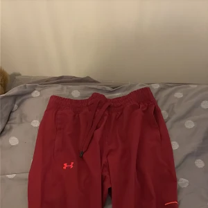 Röda träningssbxyor från Under Armour - Säljer ett par röda träningsshorts från Under Armour i storlek L. De har elastisk midja med snörning och är tillverkade i ett lätt syntetmaterial. Perfekta för gymmet eller löprundan, med klassisk UA-logga framtill.