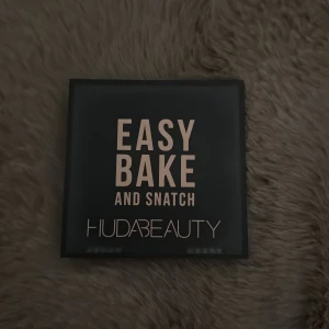 Huda Beauty Easy Bake Peach Pie puder - Pressat setting- och brighteningpuder i färgen Peach Pie från Huda Beauty. Kommer i en snygg svart fyrkantig dosa med spegel och medföljande svamp. Perfekt för att fixera sminket och ge en fräsch, matt finish. Färgen är ljus persikotonad.