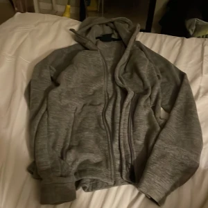 Grå fleecehoodie från Everest XS - Mjuk och varm grå hoodie från Everest i storlek XS. Tröjan har huva, dragkedja framtill och är tillverkad i gosig fleece som är perfekt när det är kyligt ute. Långärmad modell med ribbade muddar för extra komfort.