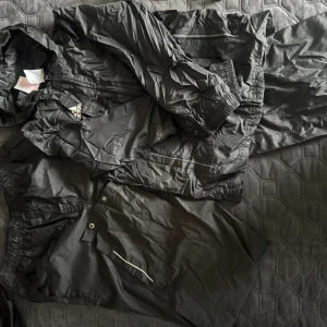 Svarta regnkläder från Crivit, stl 146/152 - Svarta regnkläder från Crivit i storlek 146/152. Byxorna är tillverkade i lätt och smidigt syntetmaterial, har resår i midjan och praktiska fickor med tryckknappar. Perfekta att packa ner i medföljande påse för enkel transport.