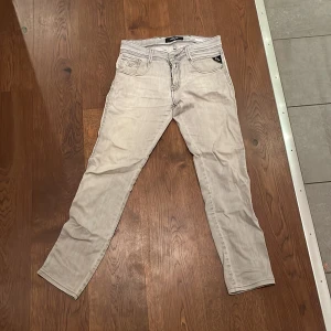 Replay Anbass  - Säljer ett par ljusgrå Replay Anbass jeans. Klassisk femficksmodell med snygga detaljer på bakfickorna och svarta kontrastsömmar. Jeansen är tillverkade i denim och har dragkedjegylf. Perfekta för dig som gillar en smalare passform. 30/34 på lappen men upplagda till ungefär 30/31≈32