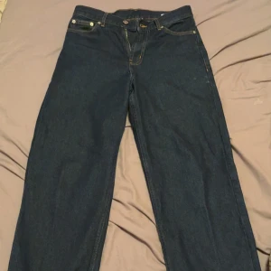 Sweet SKTBS mörkblå jeans med tryck - Mörkblå jeans från Sweet SKTBS med raka ben och gul grafisk text på bakfickorna. Klassisk femficksmodell med kontrastsömmar och knappgylf. Perfekt för dig som gillar streetwear och vill sticka ut med coola detaljer.