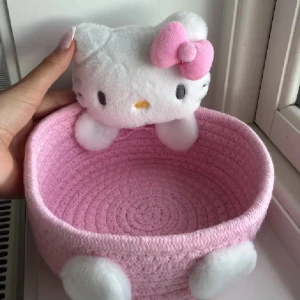 Hello Kitty rosa korg - Supergullig korg i rosa med Hello Kitty-detalj upptill och mjuka vita tassar. Väskan har en stickad struktur och en söt rosa rosett på Hello Kittys huvud. Perfekt för dig som älskar kawaii och vill ha något unikt.