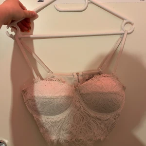 Vit spetsig korsettopp från Amisu - Säljer en vit korsettopp från Amisu med vacker spets och tunna axelband. Toppen har vadderade kupor, dragkedja bak och detaljerad spets över hela ytan. Perfekt för dig som vill ha en feminin och trendig look.