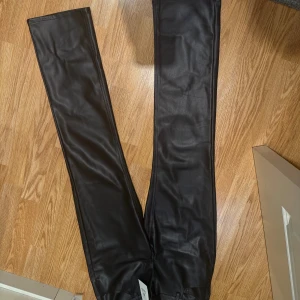 Svarta straight byxor i skinnimitation Bik Bok - Snygga svarta byxor från Bik Bok i skinnimitation med wide passform och hög midja. Byxorna har klassiska bakfickor och bälteshällor, vilket ger en cool och trendig look. Perfekta för dig som vill sticka ut med en edgy stil.