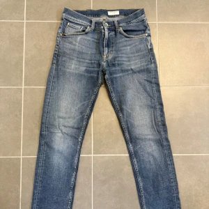 Tiger of Sweden blå jeans Leon 30/32 - Snygga blå jeans från Tiger of Sweden i modellen Leon. Jeansen har klassisk femficksdesign, normal passform och raka ben. Materialet är slitstarkt denim i bomull med snygga slitningar och ljusare partier framtill. Perfekta för en stilren och avslappnad look.