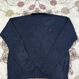  Mörkblå stickad tröja Polo Ralph Lauren - Klassisk mörkblå stickad tröja från Polo Ralph Lauren med den ikoniska röda loggan på bröstet. En tidlös och bekväm modell som passar perfekt både till vardags och till mer uppklädda tillfällen. Tröjan har två små hål, men de syns knappt när man har den på.  Längd från axeln och ner: 70 cm Bredd under armhålorna: 60 cm  📦 Skickas snabbt & välpackat.