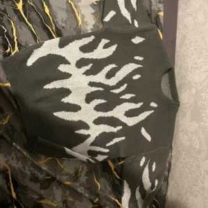 Grå stickad tröja med vit zebra-mönster - Cool stickad tröja i mörkgrått med vit zebra-inspirerat mönster över hela plagget. Tröjan har rund hals och långa ärmar med ribbade muddar vid ärmslut och nederkant. Perfekt för dig som gillar djurmönster och vill ha en unik look.