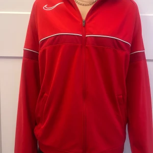 Röd Nike ziptröja Dri-Fit XL (Barn) - Nike Dri-Fit ziptröja i rött med vita detaljer och dragkedja framtill. Sportig look med lång ärm, ståkrage och fickor på sidorna. Perfekt för träning eller chill. Tillverkad i lätt polyester som andas. Köpt i USA, men behöver inte den då jag har liknade. De går att buda på 🥰 Passar även vuxna med storlek XS