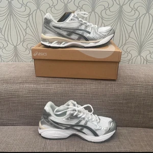 Asics Gel-Kayano 14 sneakers silver/vit - Säljer ett par Asics Gel-Kayano 14 sneakers i silver och vitt med grå detaljer. Skorna har mesh-ovandel, syntetpaneler och en chunky sula med svart och grått mönster undertill. Klassisk snörning och rund tå. Perfekta för dig som gillar sportig och retro stil.