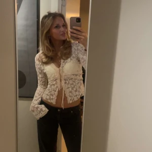 Vit spetsig croppad blus med knyt - Säljer en superfin vit blus i spets och långa ärmar. Toppen har v-ringning och snygg knytning framtill. Perfekt för dig som gillar romantisk och trendig stil med transparenta detaljer.