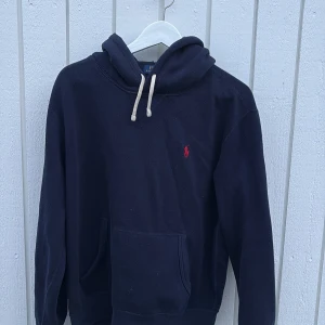 Mörkblå hoodie från Polo Ralph Lauren - Snygg mörkblå hoodie från Polo Ralph Lauren med klassisk röd broderad logga på bröstet. Använd ca ett halv år men få tal gånger. Köpt ny hos care of Carl och storlek medium passar även S!