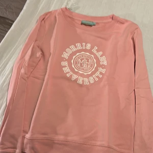 Rosa långärmad tröja Morris Lady - Snygg rosa långärmad tröja från Morris Lady med tryckt universitetslogga i vitt på bröstet. Tröjan har rund hals och är gjord i mjuk bomull, perfekt för chill dagar. Paris-vibbar och coolt college-tryck gör den extra trendig.