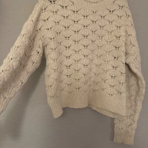Beige stickad tröja med hålmönster - Säljer en beige stickad tröja med snyggt hålmönster. Tröjan har långärmade ärmar och en rund halsringning. Perfekt för dig som gillar en chill och mysig stil.