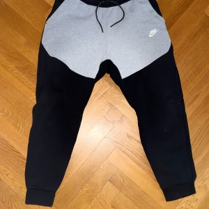 Nike tech svart och grå - Nike tech mjukisbyxor i svart och ljusgrått. Haft dom något år men har växt ur dom då dom inte passar mig lika bra längre. Skicket är utmärkt då de inte finns något tecken på skador! Passar bäst på Storlek M-L