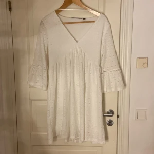 Vit kort klänning med volangärm från Vero Moda.  - Säljer en söt vit kort klänning med broderade detaljer och v-ringning. Perfekt till skolavslutning och andra tillfällen. Använd en gång på skolavslutning men har inte hittat annat tillfälle. Jag har sytt om den i midjan så att den får lite mer figur. 